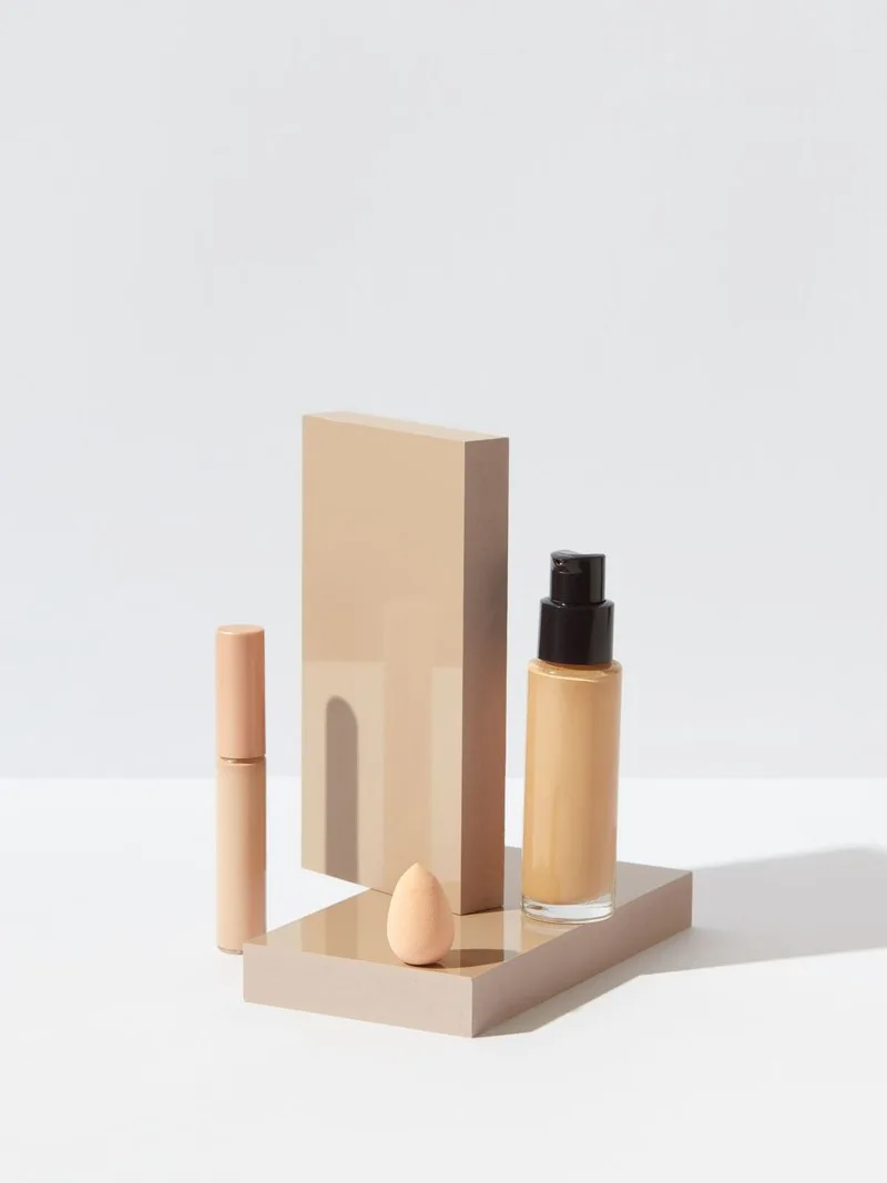 Botol alas bedak, concealer, dan spons di atas alas krem