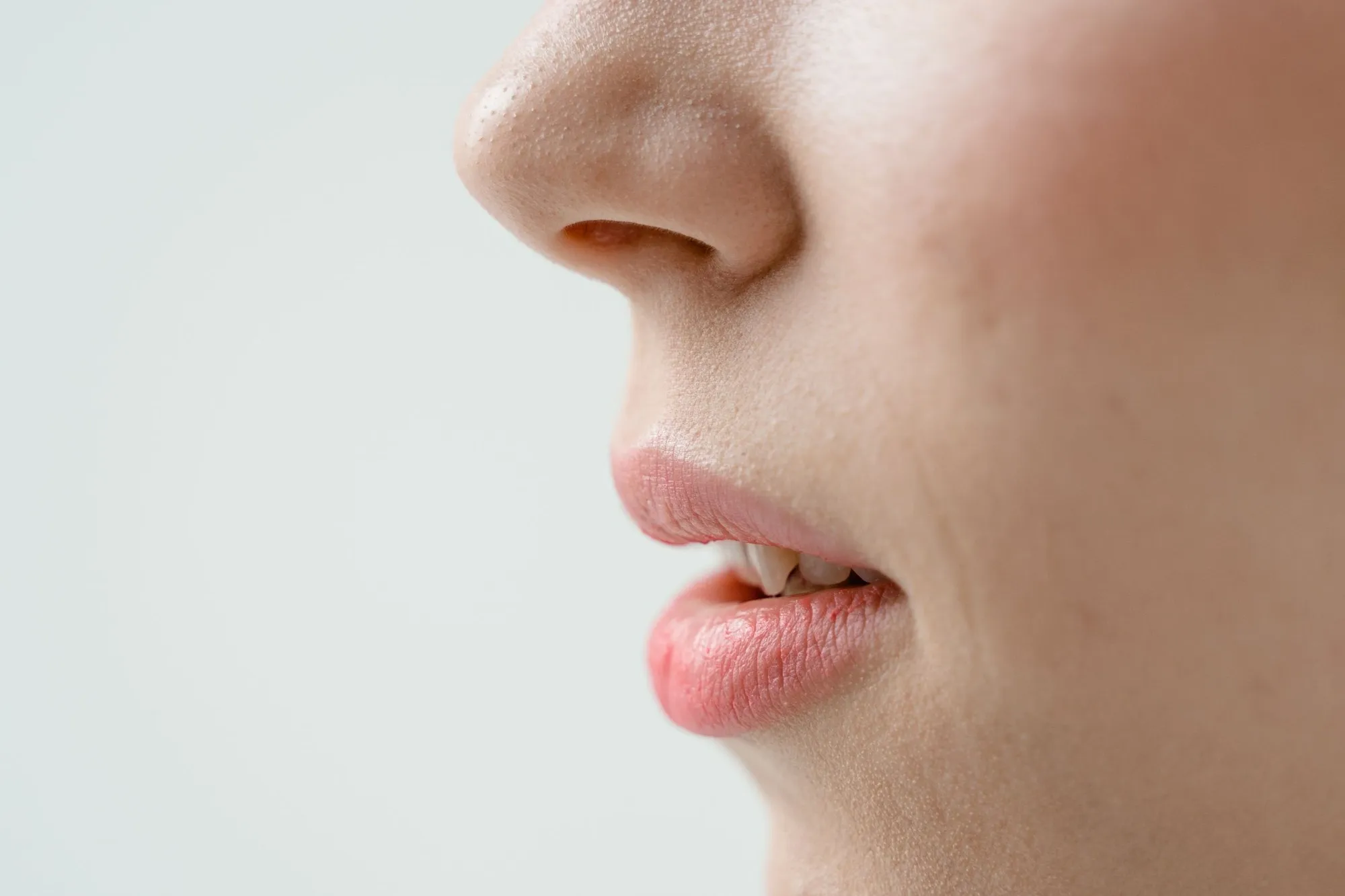 Bibir dan dagu seorang perempuan dari samping, dengan pewarna bibir merah muda